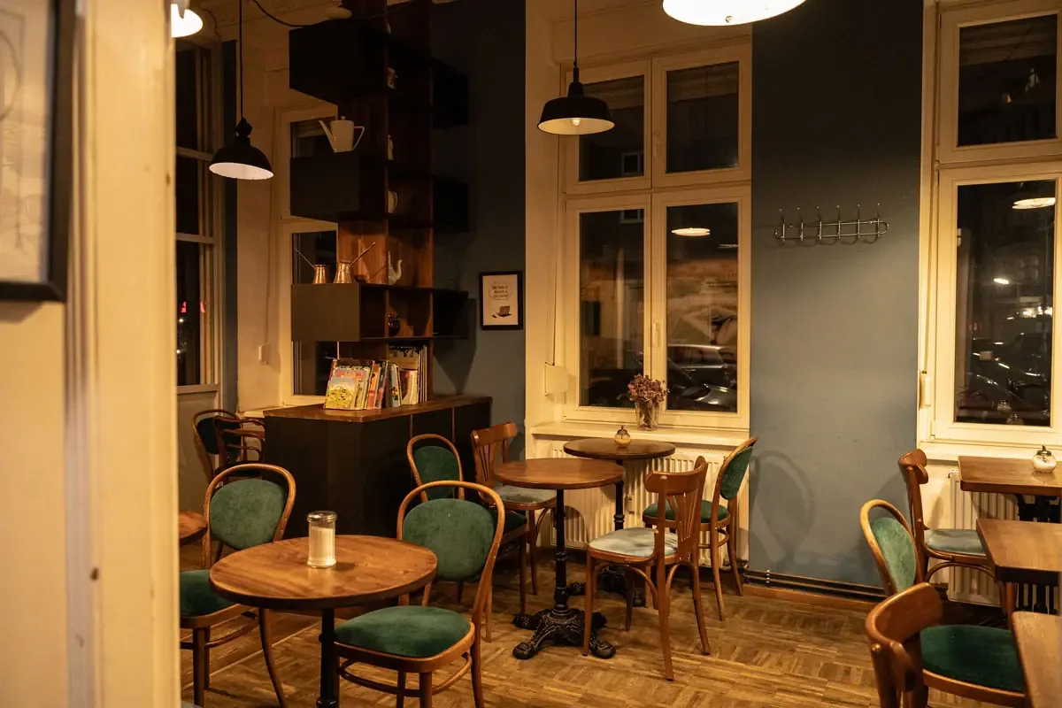 cozy café interior with wooden tables, green chairs, and pendant lighting at night., café de enrico, berlin