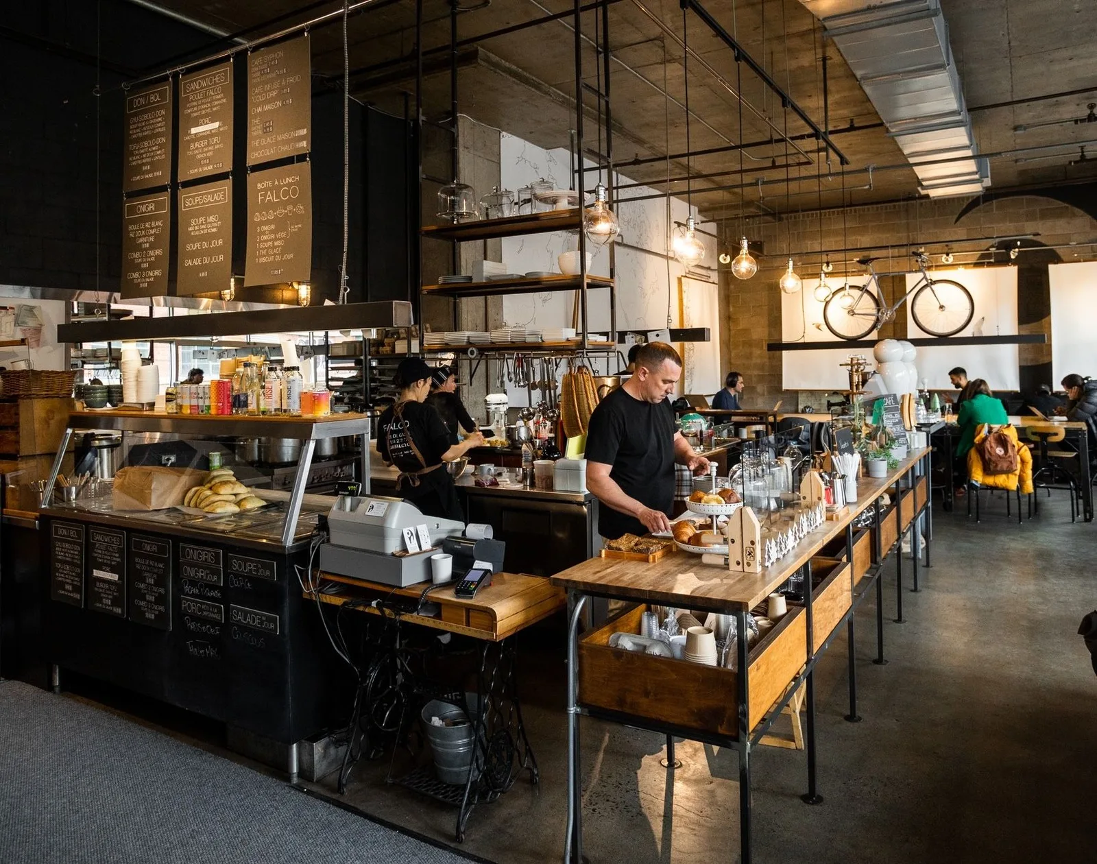 modern industrial cafe with wooden counters, staff preparing food, hanging bicycles overhead., café even, montreal