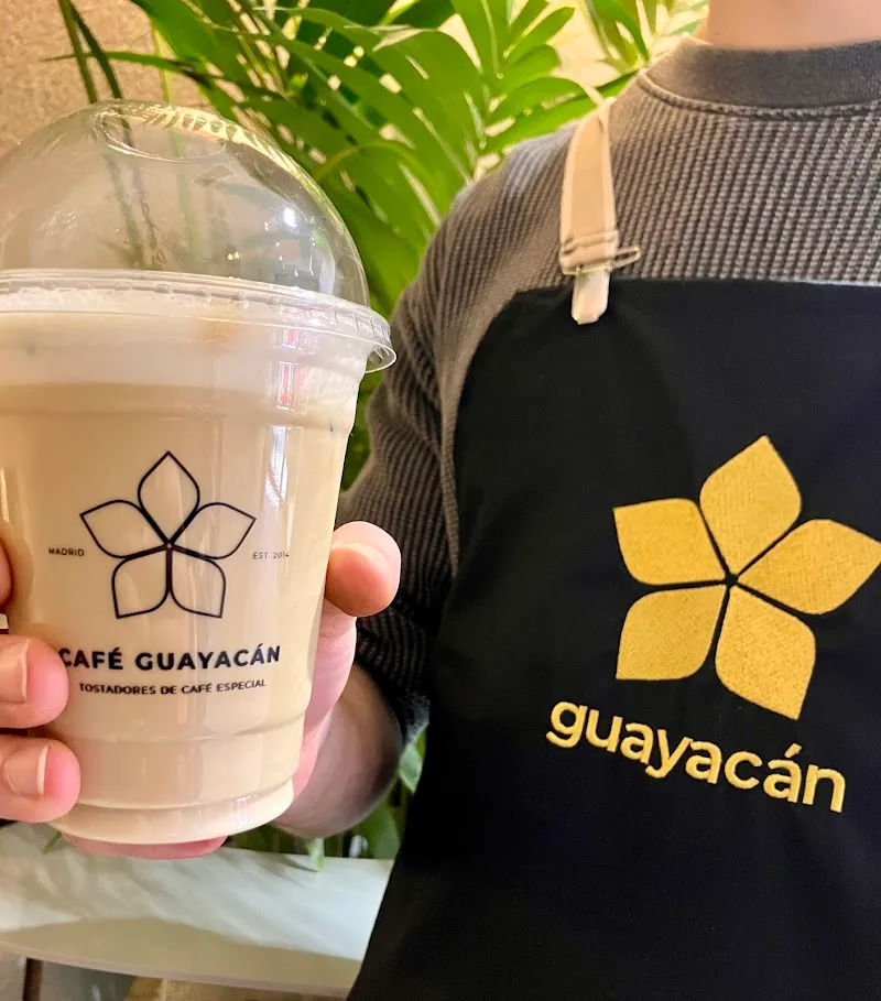 person holding café guayacán beverage cup wearing matching branded black apron., café guayacán, madrid