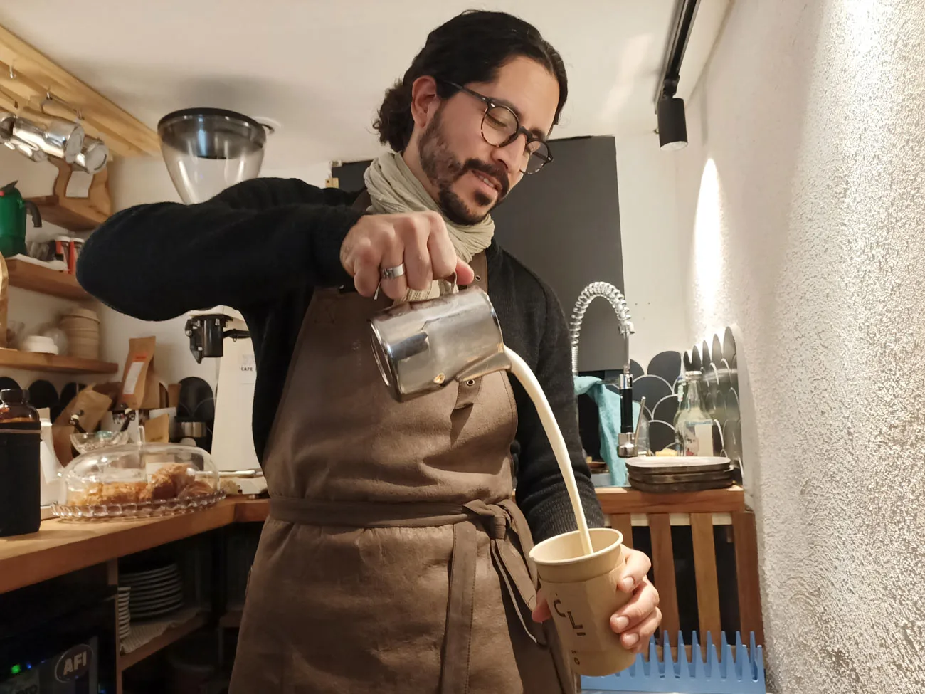 man pouring steamed milk into cup while wearing apron in coffee shop., café lauca « la boutchica », marseille