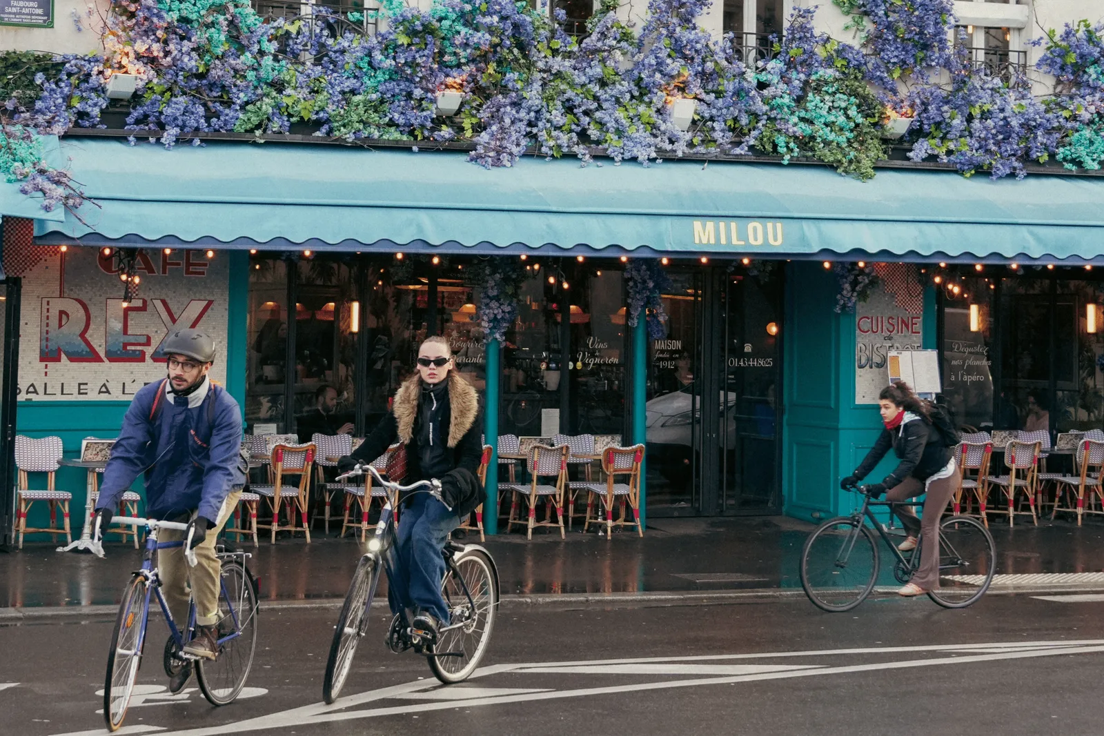 parisian café storefront with cyclists passing, purple wisteria cascading overhead., café milou bastille, paris