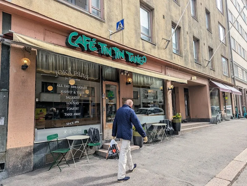 street-level café storefront with teal signage, outdoor seating, pedestrian walking past., café tin tin tango, helsinki