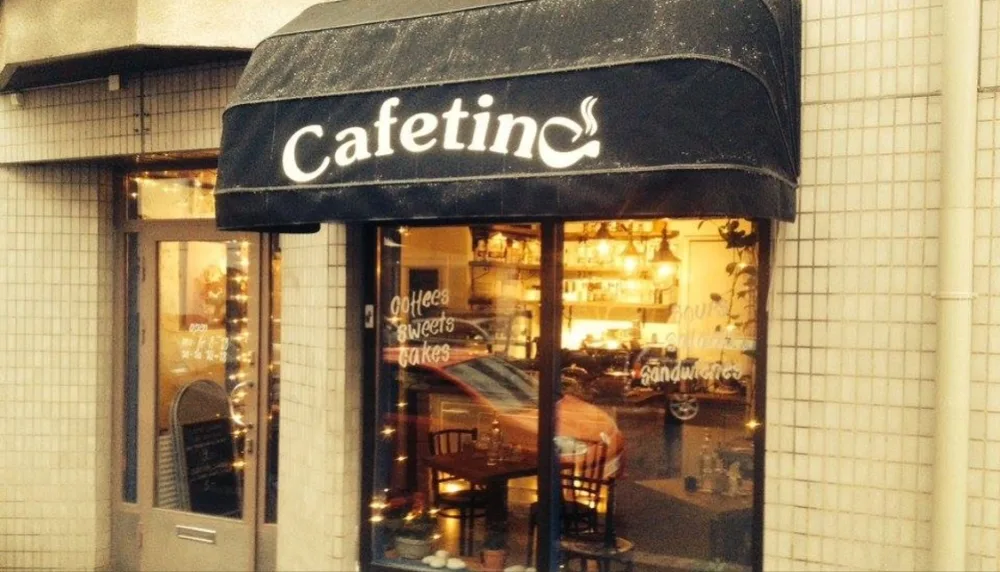 cafeteria storefront with black awning, illuminated windows displaying interior seating and warm lighting., cafetino, helsink
