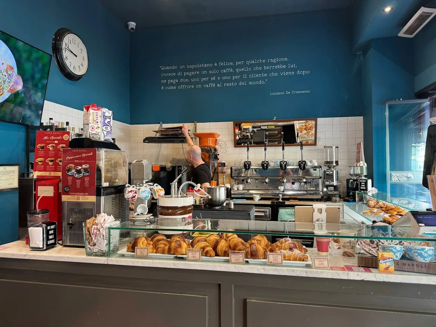 italian café counter with croissants, espresso machine, and neapolitan quote on blue wall., caffè napoli vitruvio, milan
