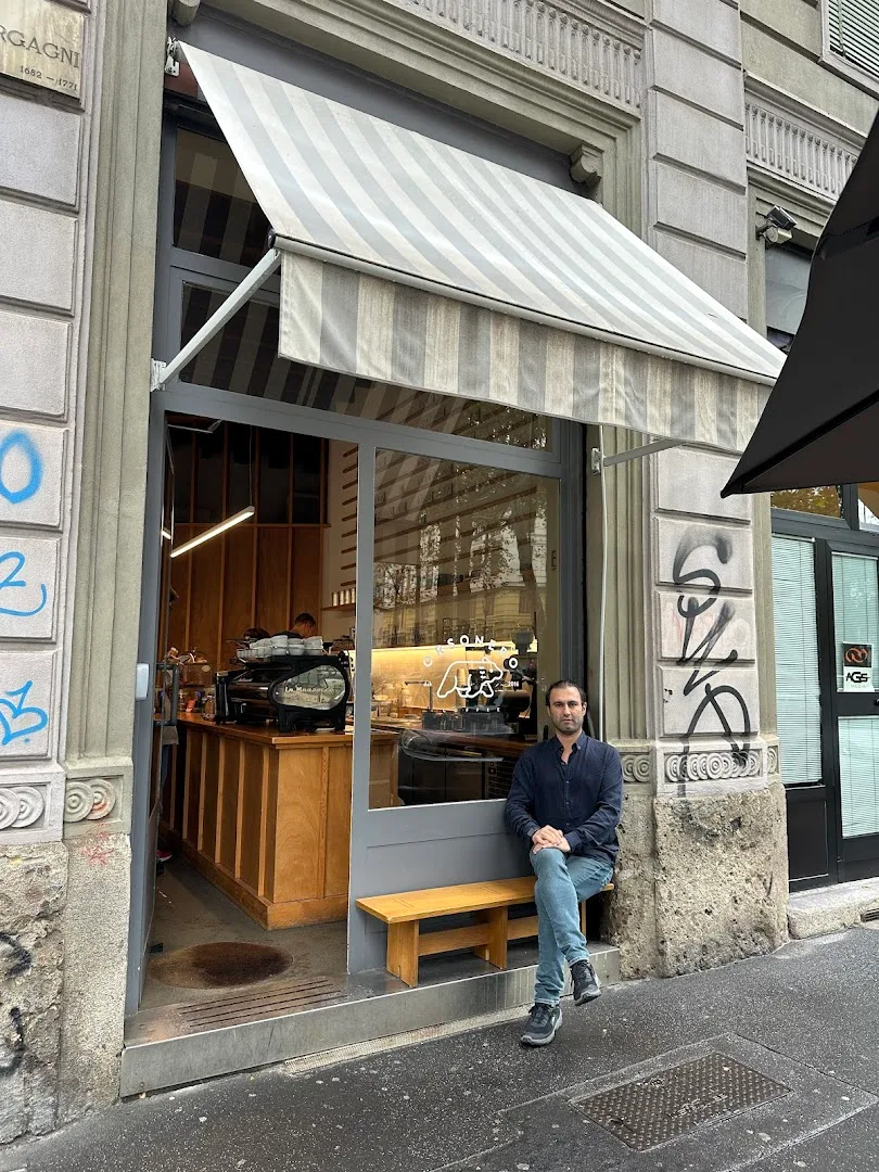man sitting outside small café storefront with striped awning., caffè napoli vitruvio, milan