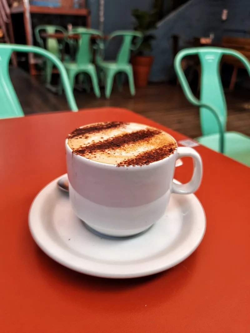 cappuccino with cocoa powder dusting on orange table, mint chairs blurred behind., caffè per tutti, curitiba