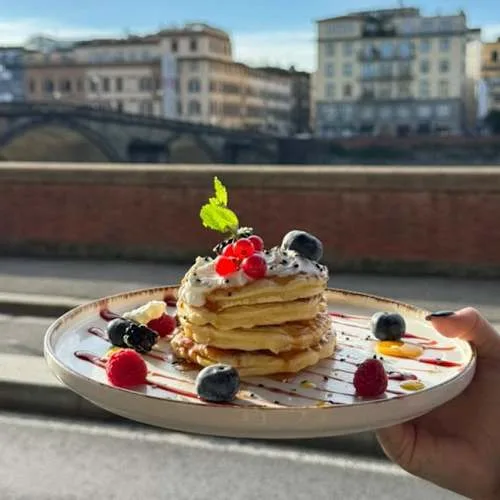 stacked pancakes with berries and cream against riverside european architecture backdrop., caffè - pizzeria del 900 firenze, 