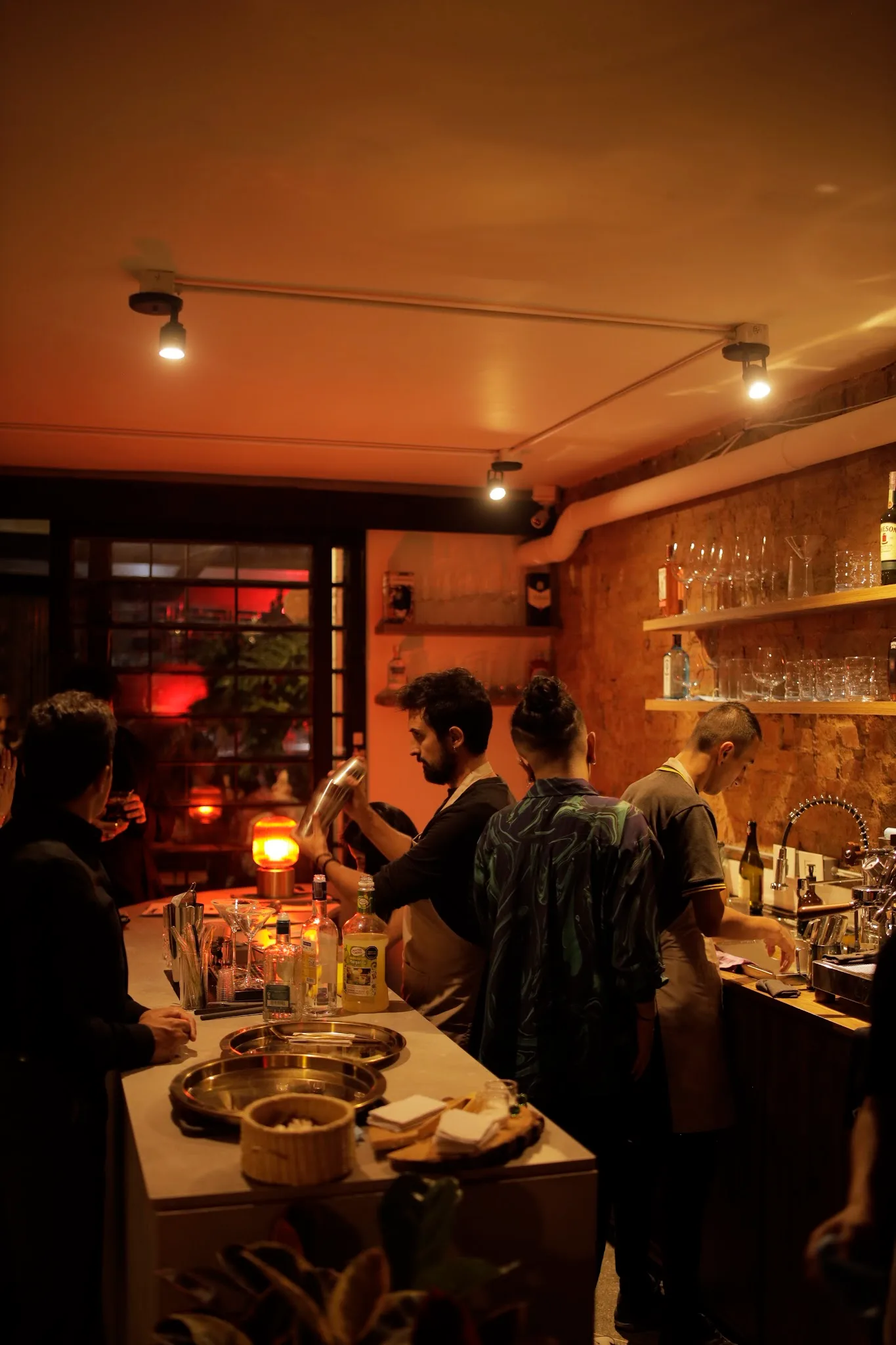 warm-lit bar interior with guests, bottles, shelves, and ambient orange lighting throughout., calma coffee & drinks, bogotá