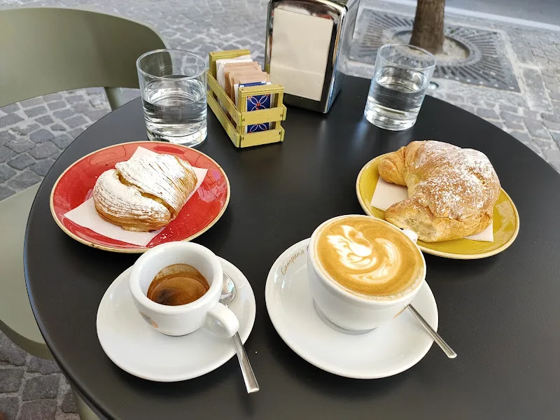 outdoor café table with pastries, espresso, cappuccino with latte art, and water glasses., campana roastery, torre annunziata