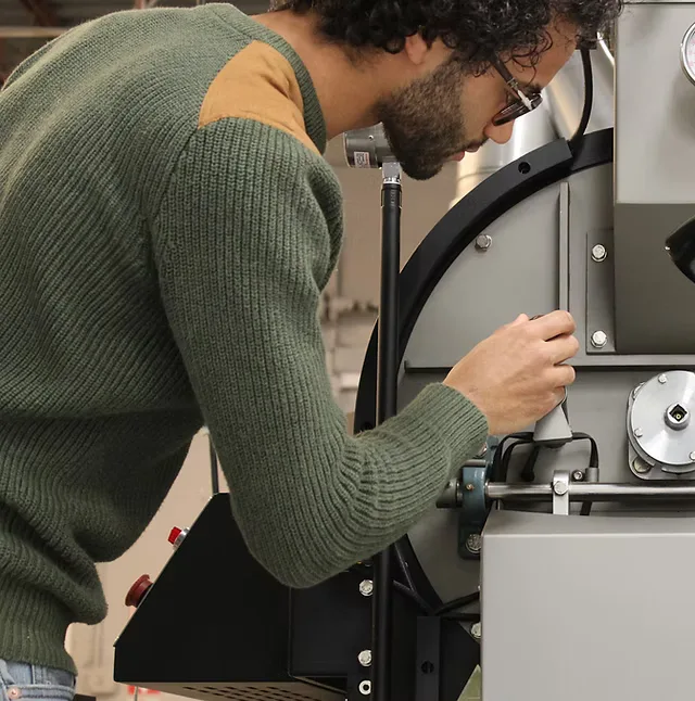 man in green sweater adjusting equipment with black cables and metal components., canvas coffee roasters, newport news