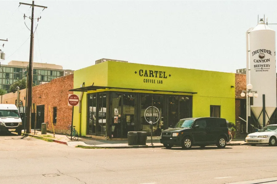 bright yellow cartel coffee lab storefront with parked vehicles and brewery tower., cartel roasting co, tucson