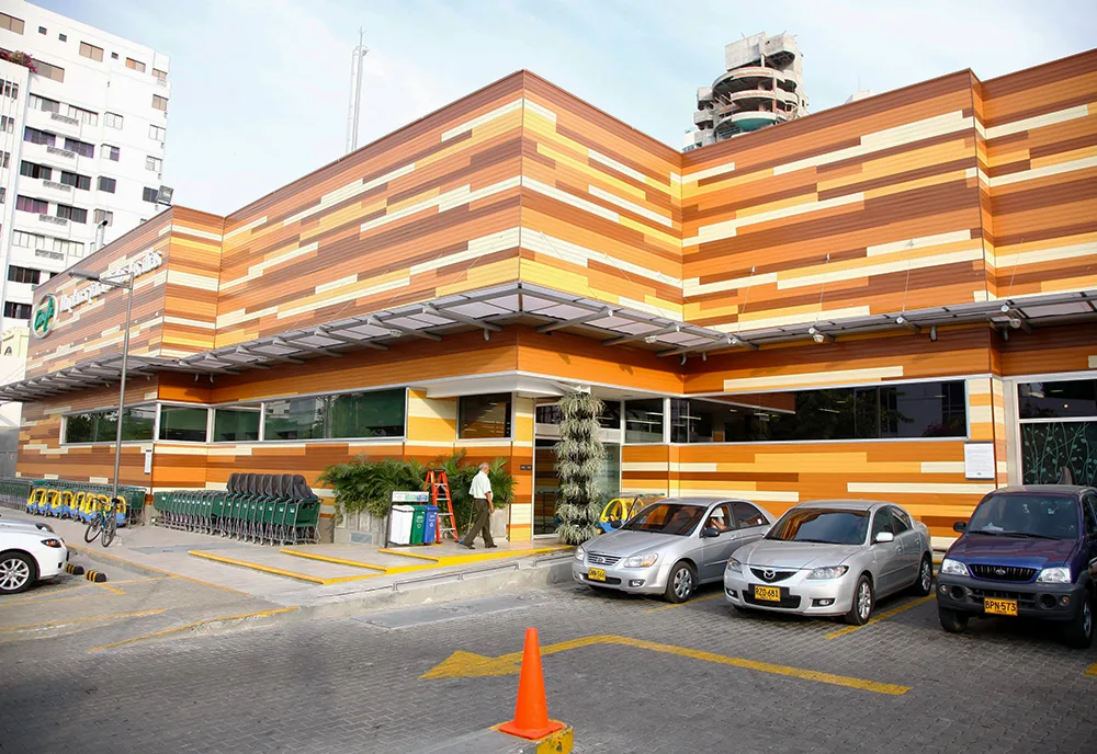 striped orange and yellow commercial building with parked cars and bike-sharing station., carulla castillo grande, cartagena