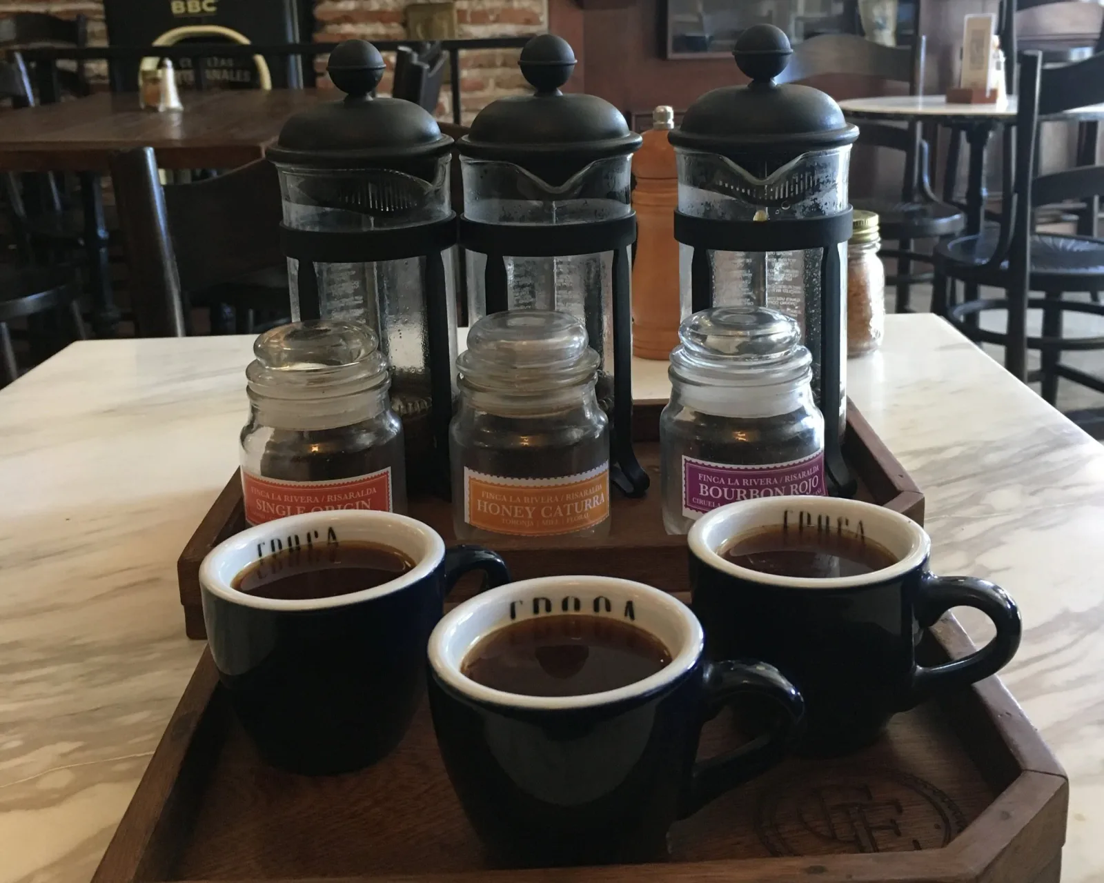 three black mugs with coffee and three glass jars with syrups on wooden trays., carulla castillo grande, cartagena