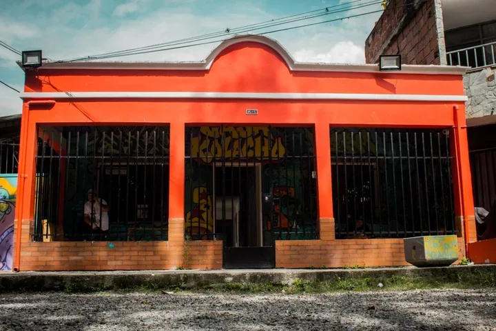 bright orange storefront with barred windows and brick base foundation., casa kolacho, medellín
