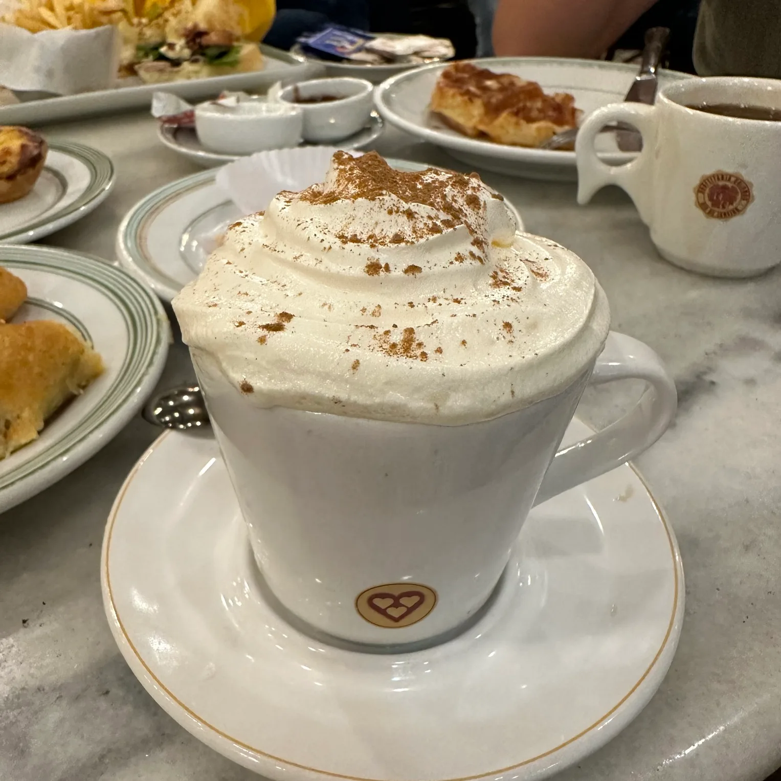 cappuccino with whipped cream and cocoa powder in elegant white cup and saucer., casa que doce, rio de janeiro