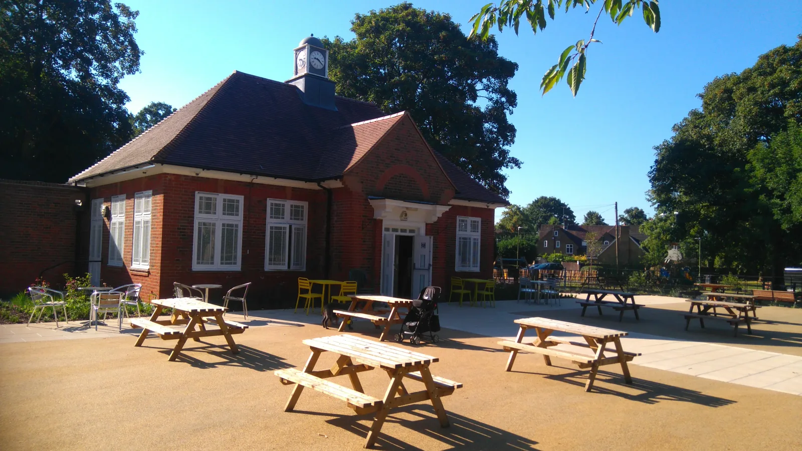 red brick building with clock tower, picnic tables, and playground in sunny village setting., cassiobury park, watford