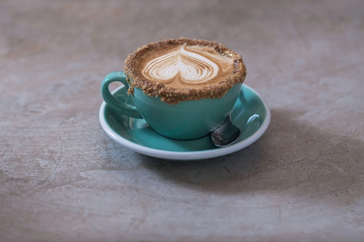 turquoise cup with latte art and cinnamon rim on white saucer., castalia bakery and cafe, brasília
