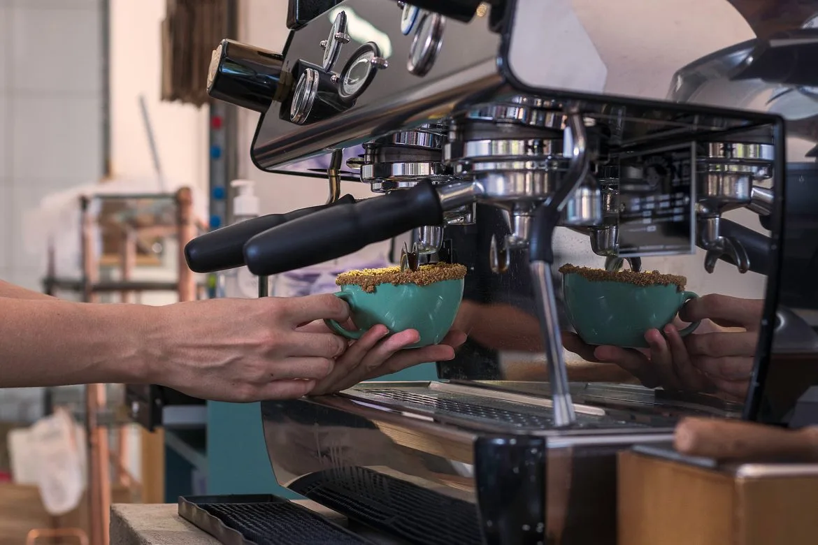 barista dispensing espresso into turquoise cups beneath dual group espresso machine., castalia bakery and cafe, brasília