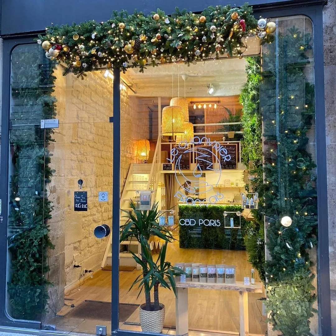 festively decorated storefront with greenery, gold ornaments, and warm lighting display., cbd paris 4 - le chanvrier francais