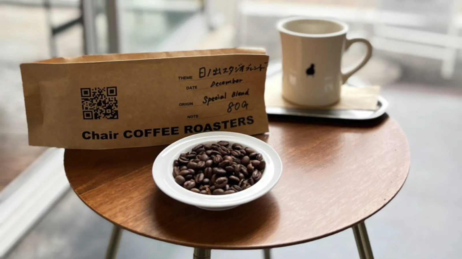 coffee beans in white bowl, branded kraft bag, mug on wooden table by window., chair coffee roasters, yokohama