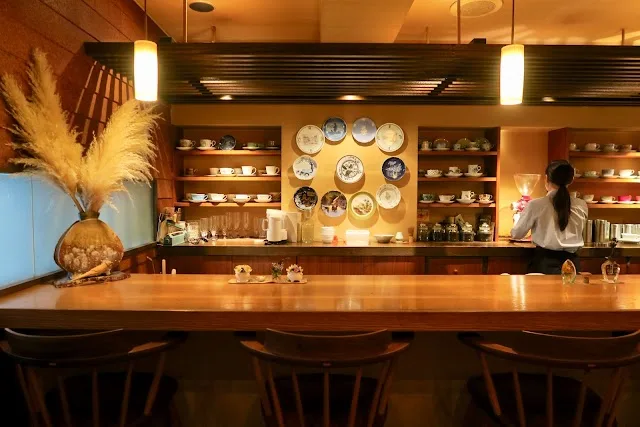 warm-lit restaurant counter with decorative plates, wooden bar seating, and shelved dishware display., charcoal roast coffee 