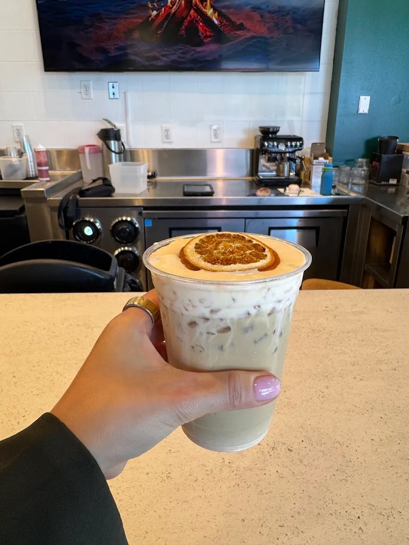 hand holding iced coffee drink with cinnamon roll pastry on top in café., chase coffee roasters, fullerton