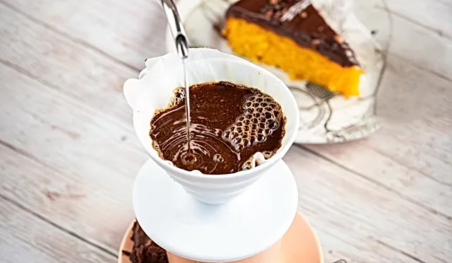 pouring hot water through coffee filter with chocolate cake slice in background., chez mom - café & confeitaria - vila madale
