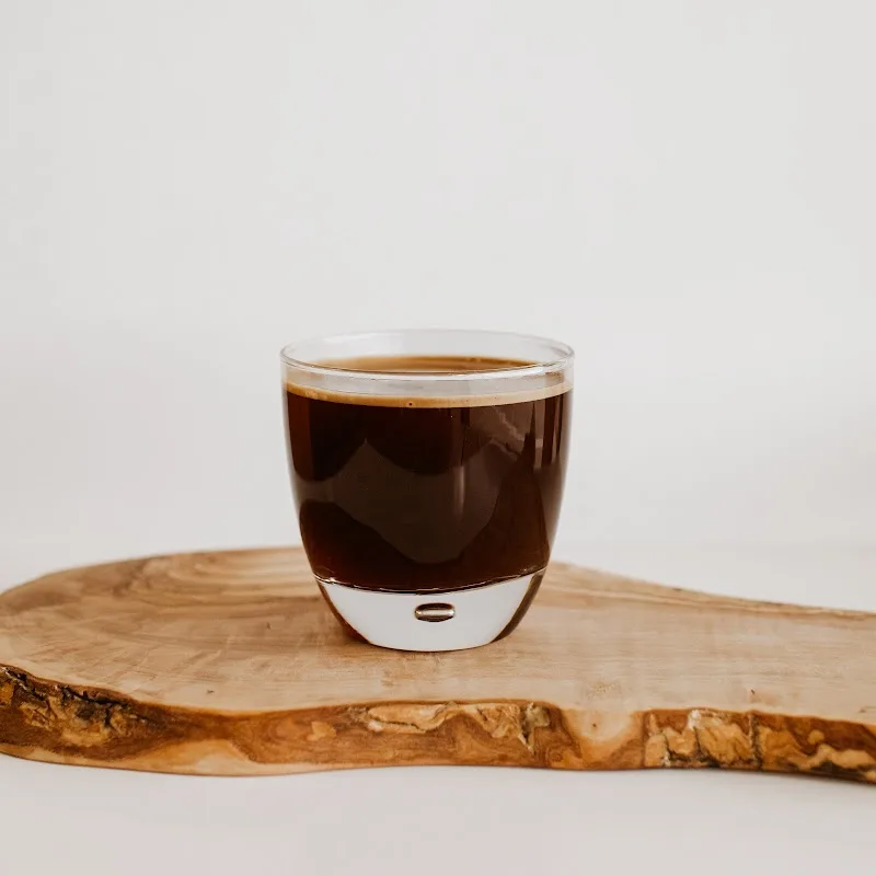 dark espresso in glass cup on natural wood slab, white background., coffee del rey, plano