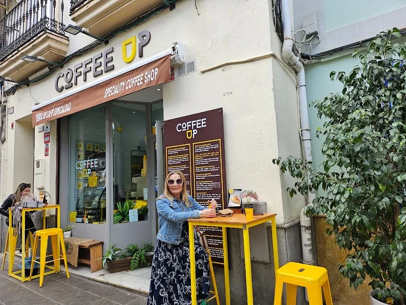 coffee shop storefront with yellow seating, woman customer, ivy-covered wall., coffee up triana - specialty coffee shop / el 