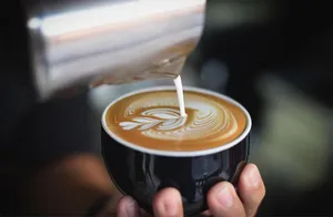 barista pouring steamed milk into espresso, creating latte art design., coffeestamp, st. louis