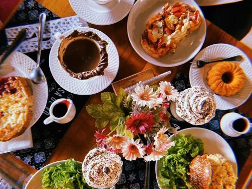 overhead spread of pastries, coffee, bagels, fresh flowers, and salads on dark table., coisa de vó, belo horizonte