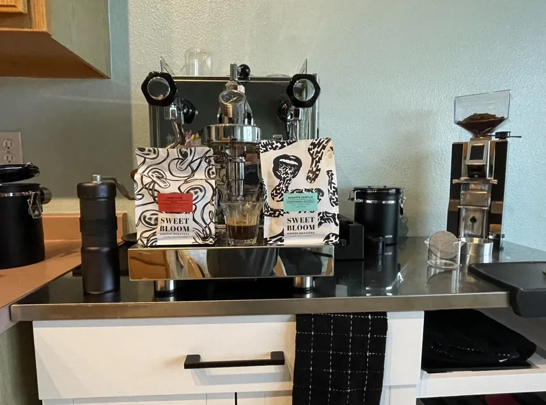 modern espresso machine setup with sweet bloom coffee bags and black accessories displayed., colorado ironcrest coffee roaste