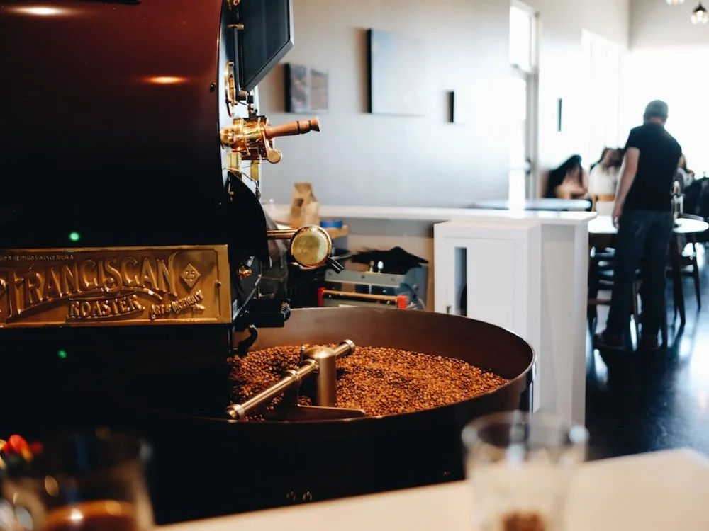 coffee roaster with roasted beans in drum, modern café interior with customers visible., colorado ironcrest coffee roasters, 