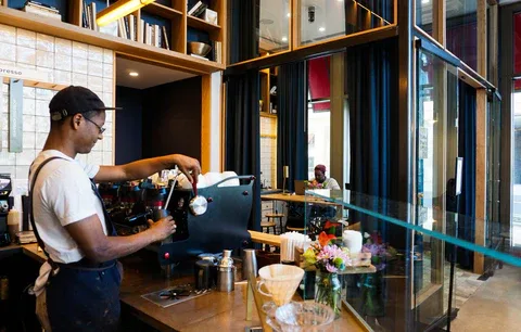 barista preparing drink at espresso machine in modern café with wooden shelving., commonwealth joe coffee roasters, washingto
