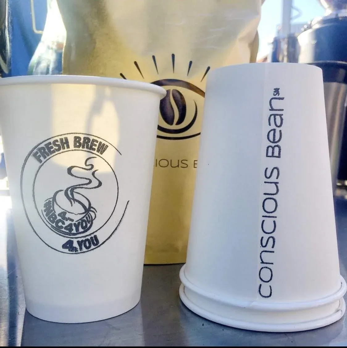 white coffee cups with "fresh brew" and "conscious bean" branding on sunny table., conscious bean coffee catering, san bernar