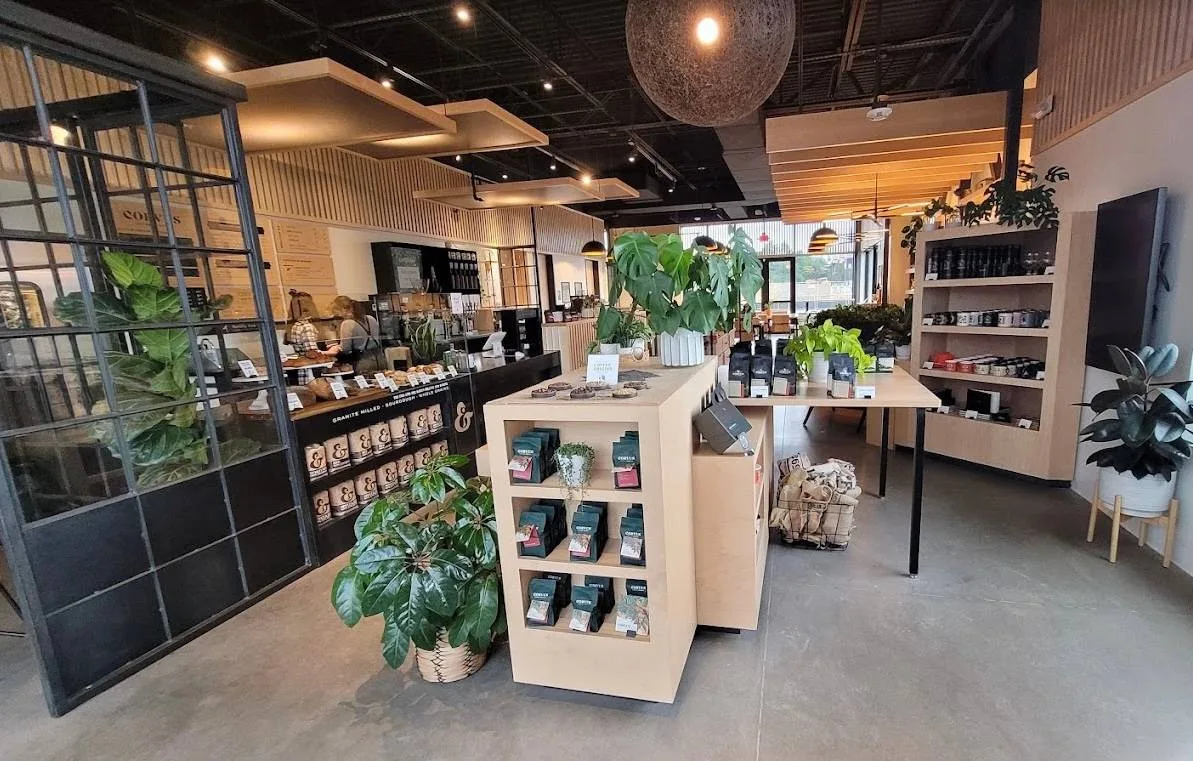 modern coffee shop interior with central display counter, shelving, and abundant green plants throughout., corvus coffee roas