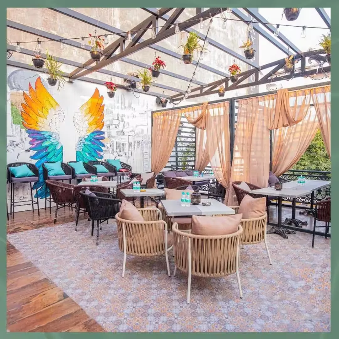 rooftop terrace with hanging plants, colorful wing mural, and lounge seating., courtyard revibe - cafe & restaurant | dwarka,