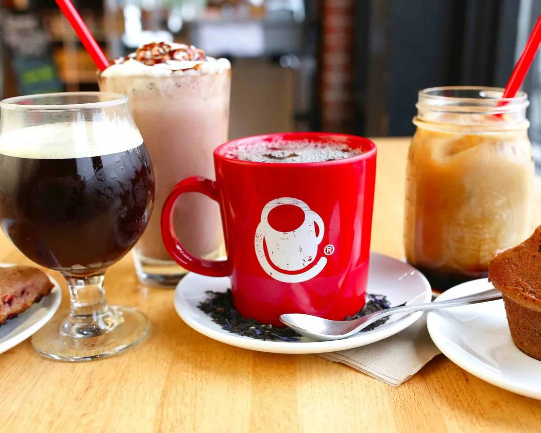 red smiley mug with beverages, pastries, and food items on wooden table., crimson cup coffee shop - upper arlington, columbus
