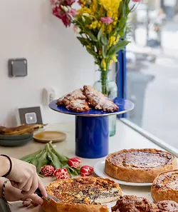 baked goods and pastries displayed with fresh flowers in blue vase by window., culottée boétie - petit déjeuner, déjeuner, br