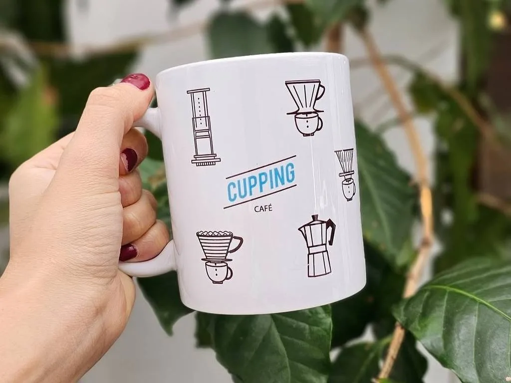 white mug labeled "cupping café" held in hand with coffee brewing method illustrations., cupping café, são paulo