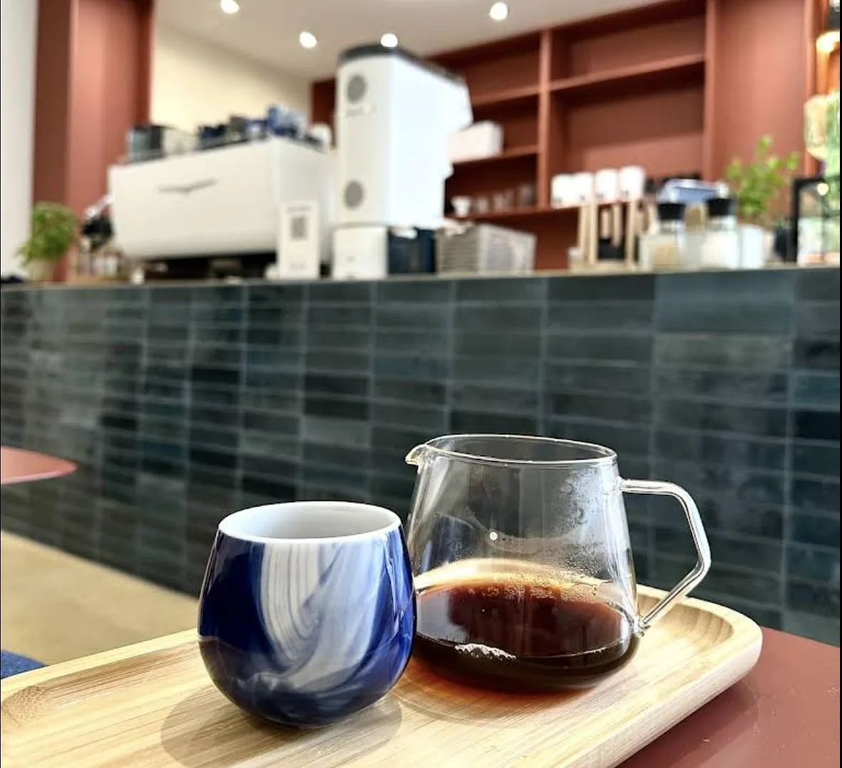 coffee shop counter with ceramic cup, carafe, and espresso machine visible behind., cusuaka cafés - boulogne centre, boulogne