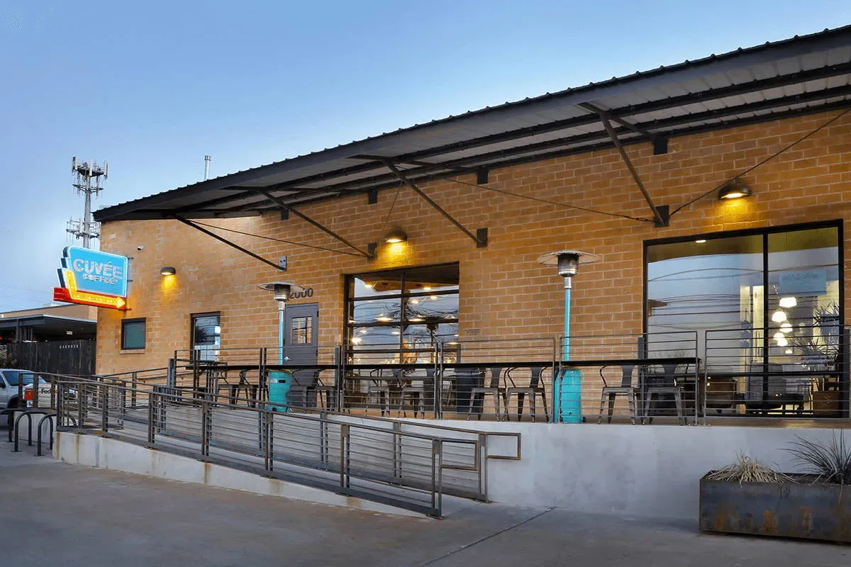 modern brick café with metal railings, illuminated signage, and outdoor seating area at dusk., cuvee coffee, austin