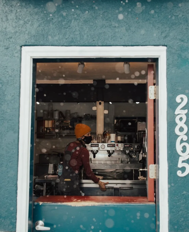 barista in orange beanie working at espresso machine in turquoise storefront., daily rise coffee ogden, ogden