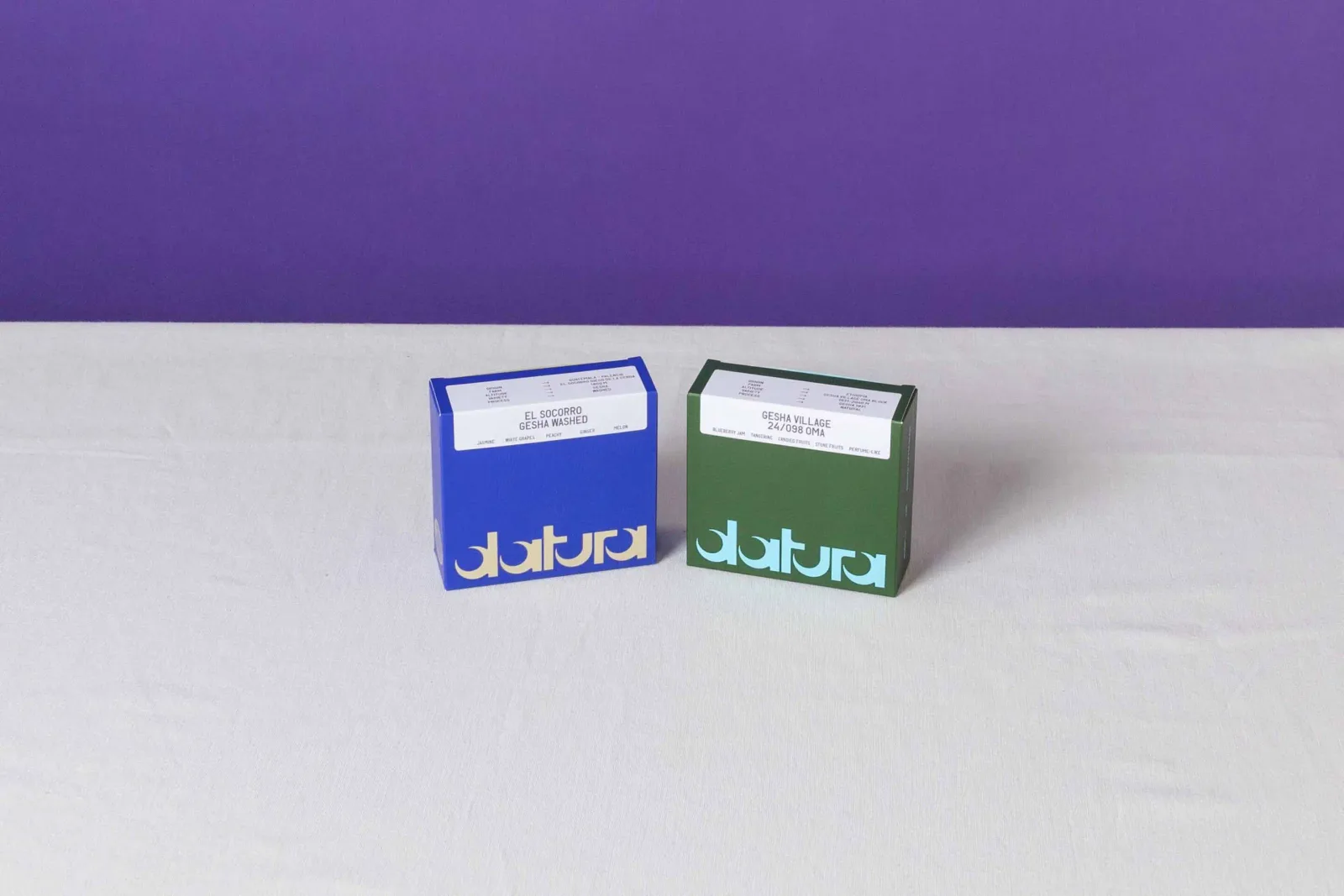 two colored boxes labeled "datura" on white surface, purple background., datura, paris