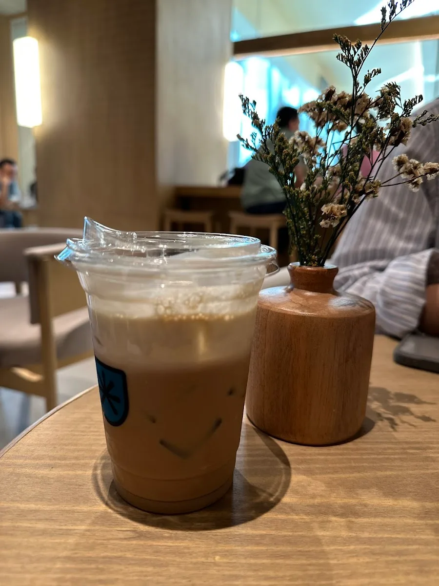 iced coffee drink on wooden table beside dried flowers in pot., djournal coffee at cafe kissa, jakarta