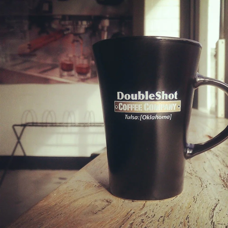 black mug from doubleshot coffee company in tulsa, oklahoma sits on wooden table., doubleshot coffee co, oklahoma