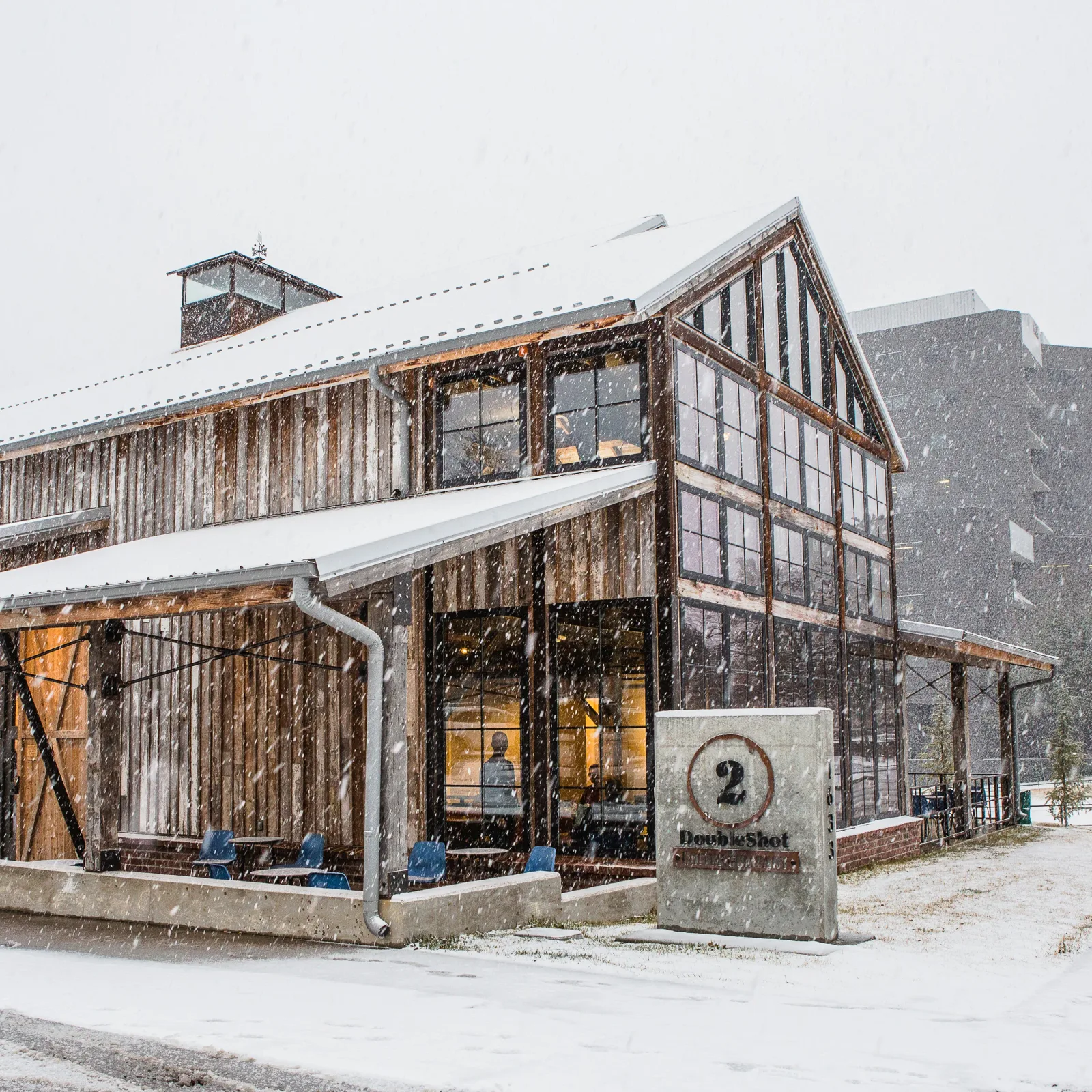 rustic industrial building with weathered wood and large windows during snowfall., doubleshot coffee co, tulsa