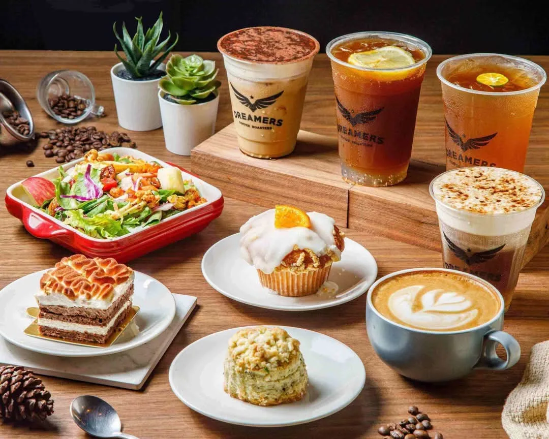 café display featuring pastries, salads, specialty coffees and cold beverages with plants., dreamers coffee roasters 南西店 | 全新