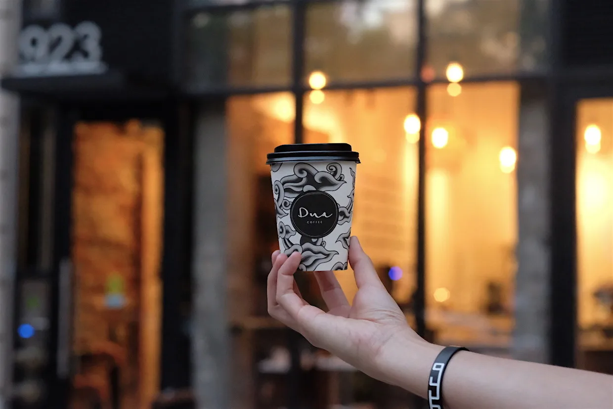 hand holding decorative coffee cup with storefront and warm lighting in background., dua dc, washington