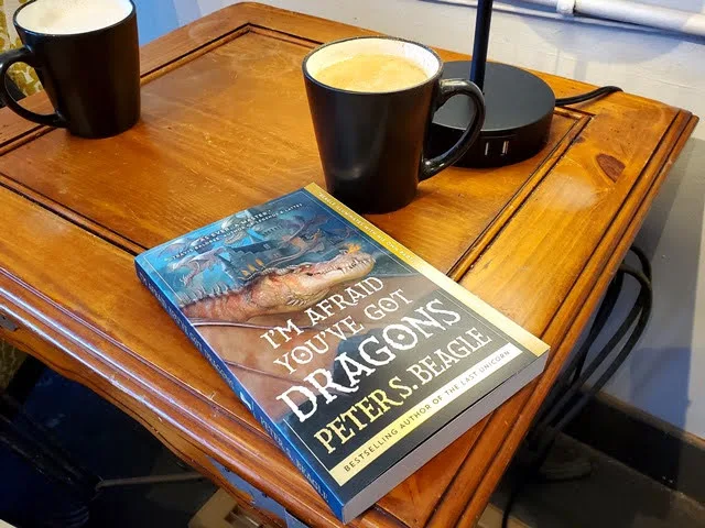 wooden desk with "i'm afraid you've got dragons" book and two steaming black mugs., dudley's bookshop cafe, bend
